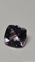 Close view of the square cushion fancy cut pink to purple amethyst gemstone on a neutral background showing clarity and facets.