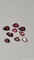 Top view of ten natural pear cut fancy pink tourmaline gemstones arranged on a neutral background showing their color range and clarity.