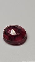 Close-up image of the oval cut opaque ruby showing deep red color and internal texture.
