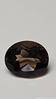 Close-up image of the dark brown oval cut natural smokey quartz gemstone showing its cut and surface reflection.