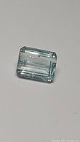 Close-up photo of a rectangular emerald cut light blue aquamarine gemstone showing transparency and slight inclusions.