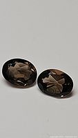 Pair of natural smokey quartz oval cut gemstones shown on white background, highlighting polished facets and brown smoky color.