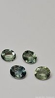 Four oval-shaped multicolored rose cut sapphires on a white background showing different green to blue hues.