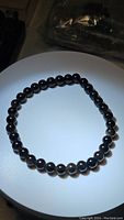 Bracelet arranged in a circle on a light surface showing black polished round beads with slight sheen.