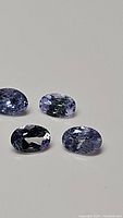 Four oval cut natural tanzanite gemstones, blue-violet color, shown from angled top view to highlight cut and clarity