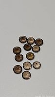 Top view of 13 round cut calibrated smokey quartz gemstones arranged on a light grey surface.