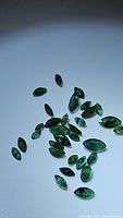 Cluster of marquis cut emeralds with visible inclusions on a plain surface with light reflection.