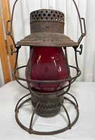Front view of antique railroad lantern with red glass globe and metal cage, displaying its full shape and condition.