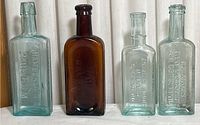 Four antique glass medicine bottles in a row, showing front embossed text and colors.