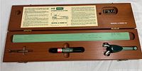 Top view of wooden case containing K-E Doric lettering set. Includes green stencil, black lettering pen, and metal tool with case lid open showing labels and instructions.