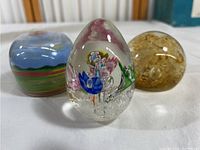 Front view of the three paperweights showing the clear floral Murano paperweight centered with two round colored paperweights behind it