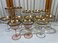 Front view showing the full collection of 14 glasses with various shapes and sizes, all with gold rims.