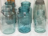 Front view showing six vintage jars of different styles and embossing, mainly Ball and Lightning brands with wire handles and one metal lid jar.
