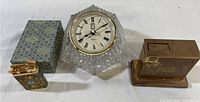 Photo showing the vintage clock, large brass-tone lighter, and small floral decorative lighter on a white surface with the original box for the small lighter.