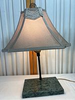 Full view of the lit table lamp showing fabric lampshade with light glow and black metal stem mounted on the green marble base.