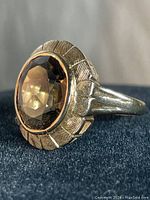 Close-up front view of yellow gold ring with brown oval stone showing the faceting and detailed engraving on bezel.