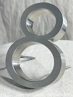 Front angled view of satin nickel house number 8, showing the smooth surface and mounting pins.