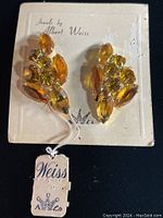 Pair of Albert Weiss vintage 1930's clasp earrings on original Weiss branded card with attached tag, showing yellow and amber colored jewel stones clustered in gold-tone metal.