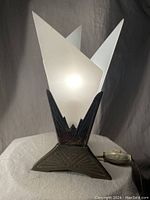 Front view of Art Deco lamp with frosted glass panels illuminated, showing brass base and electrical cord with inline switch.