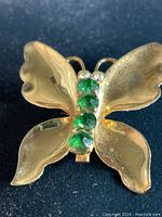 Front view of vintage Coro Craft butterfly brooch featuring gold-tone sterling wings and three green stones on the body with two small clear stones as eyes.