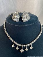 Full view of the rhinestone choker necklace with dangling square rhinestones and matching clip-on earrings displayed on black velvet stand.