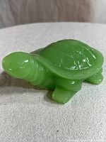 Side view of a green jadeite turtle figurine showing detailed sculpting on the head, legs, and shell.
