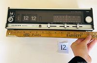 Front side of the Lloyds flip clock radio alarm clock showing the flip clock numbers and AM/FM radio tuning scale with control sliders and knobs visible.