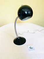 Front view of the black eyeball desk lamp showing the lamp head, flexible gooseneck, and round base with power cord.