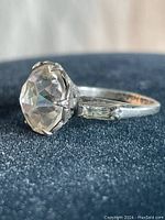 Side view of vintage sterling silver ring showing large round clear center stone and one baguette-cut clear side stone attached to the band