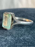 Close-up side angle of vintage sterling silver ring with faceted lime green rectangular stone on a black surface.