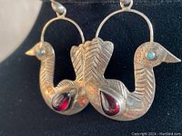 Front view of the pendant showing the double-headed bird design with garnet stones and turquoise eyes.