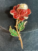 Front view of vintage Trifari rose pin showing red enamel petals, green enamel leaves, clear rhinestone accents, and faux pearl on gold tone metal.