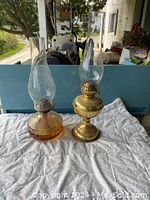 Both antique kerosene lamps together showing amber glass and brass bases with chimneys