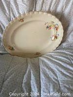 Photo of a large oval antique china platter with small floral pattern on scalloped rim, placed on soft fabric surface.