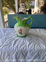 Full view of the ceramic antique reproduction jug showing green top section, white body, floral details, and ornate handle.