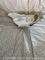 Gravy boat with blue floral pattern and gold accents on cream ceramic, placed on fabric background