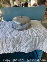 Image showing glass cake plate with silver plate dome cover on a white cloth with blue background