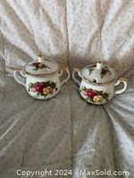 Two Royal Albert Country Rose sugar bowls with lids displayed on fabric.