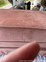 Close-up of pink velvety fabric top and side of foot stool hassock, showing texture and some dust.