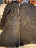 Men's black leather coat laid out flat showing front with zip closure and pockets