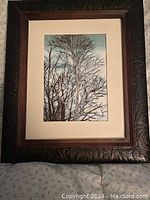 Front view of framed fabric artwork showing birch trees in winter against a blue sky background with an ornate dark brown carved wooden frame and cream matting.