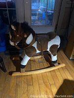 Side view of the toy rocking horse showing brown and white plush covering, black mane, leather saddle and stirrups on light wood rockers.