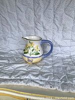 Front view of large ceramic jug with herb garden hand-painted motif, blue handle, yellow flowers and butterfly.