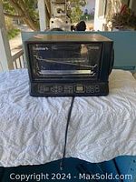 Full view of black Cuisinart toaster oven with front glass door, digital control buttons, and display screen visible, placed on white cloth.