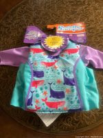 Photo showing the full floatation device with rash guard, colorful whale and starfish marine print, purple sleeves, turquoise sides, and brand tags.