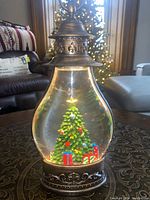 Front view of battery operated festive lantern with Christmas tree and presents inside glass enclosure on table