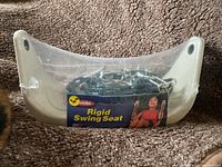 Photo of the rigid swing seat in original packaging showing the seat and chain inside on a textured surface.