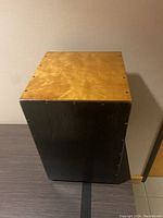 Front view of wooden cajon drum box showing natural wood finish seating surface and black sides.