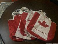Eleven Canada-themed handbags stacked showing red and white design with maple leaf and CANADA text.