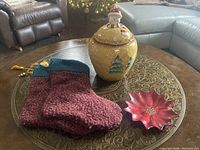 Photo showing the full lot: ceramic cookie jar with snowman lid, two knitted stockings, and red poinsettia plate on a table.